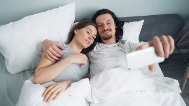 Barbudo cara tomando selfie na cama com namorada usando câmera de smartphone — Vídeo de Stock