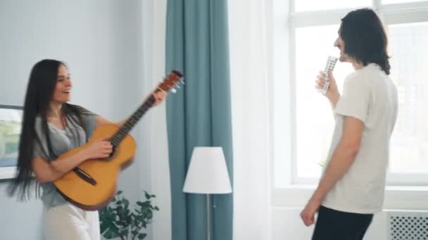 女孩和家伙唱歌弹吉他和跳舞在床上在公寓 — 图库视频影像