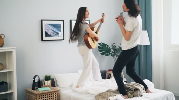 Donna suonare chitarra ragazzo cantare in telecomando e ballare sul letto a casa — Video Stock