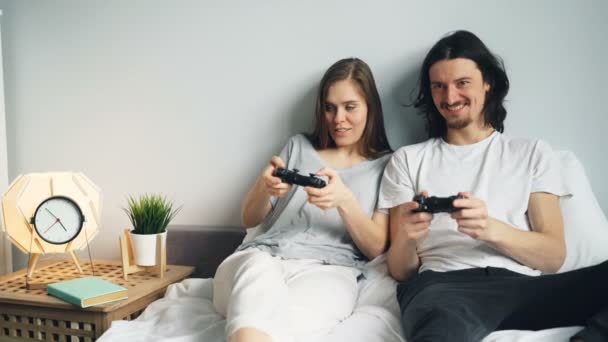 Aranyos fiatal pár barátja és barátnője játszik videogame ágyon otthon — Stock videók