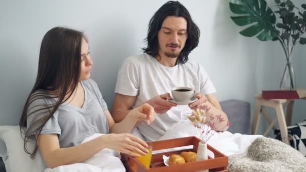 コーヒーフルーツジュースペストリーと自宅でベッドで朝食を持つ美しいカップル — ストック動画
