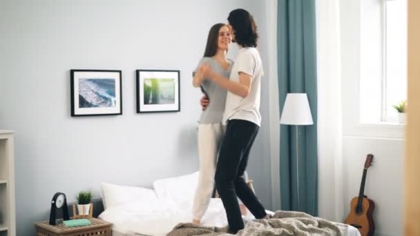 Adorable pareja amorosa bailando en la cama en casa abrazándose divirtiéndose — Vídeos de Stock