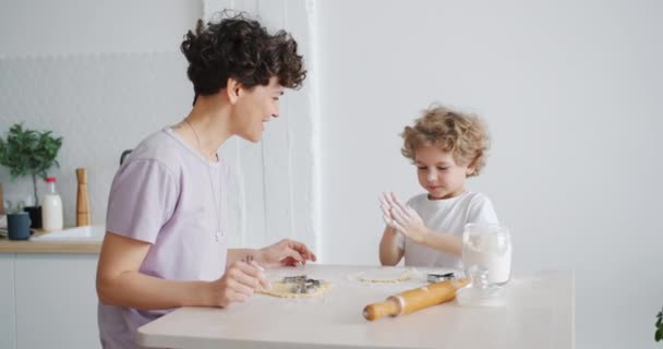 Lindo niño aplaudiendo las manos cubiertas con galletas de harina de cocina con mamá en la cocina — Vídeos de Stock