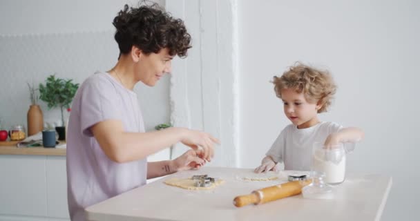 Jonge vrouw en kleine jongen zetten meel op deeg dan plezier in de keuken — Stockvideo