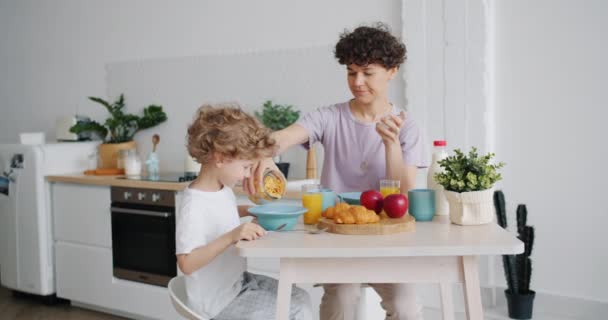 Evde mutfakta küçük oğlu için tabağa mısır gevreği koyarak annenin yavaş hareket — Stok video