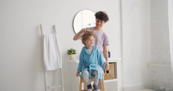 Fürsorgliche Mutter bürstet lockiges Haar eines entzückenden Jungen im Badezimmer zu Hause — Stockvideo