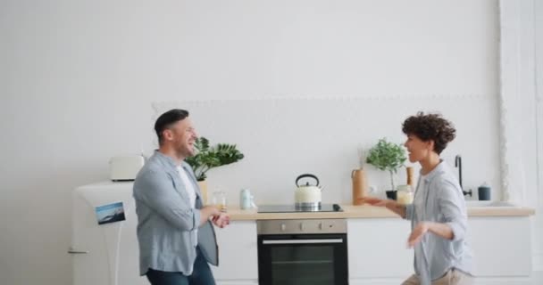 Χαρούμενο ζευγάρι άντρας και γυναίκα που χορεύουν στο σπίτι στην κουζίνα που διασκεδάζουν μαζί — Αρχείο Βίντεο