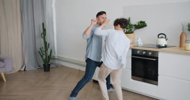 Guy singing in spoon dancing in kitchen with wife having fun enjoying music — Stock Video