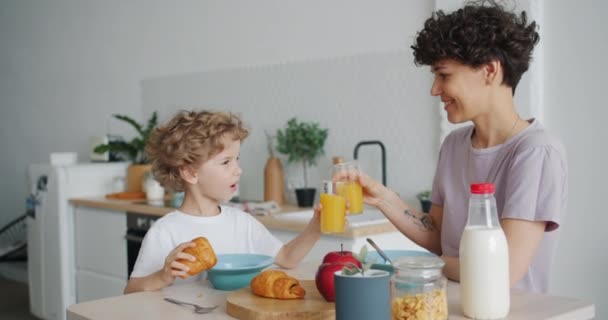 Familia feliz madre e hijo bebiendo jugo de naranja y comiendo croissants en casa — Vídeos de Stock