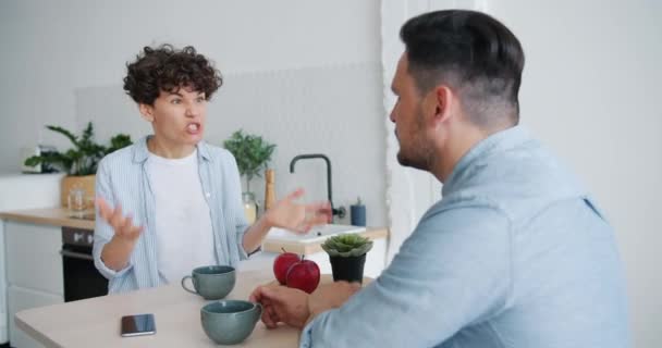 Mouvement lent de la femme en colère se disputant avec le mari à la maison à la table de cuisine — Video