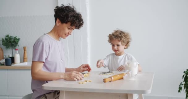 Joven familia madre e hijo haciendo galletas en la mesa de la cocina trabajando con masa — Vídeos de Stock