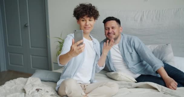 Young couple making video call with smartphone talking showing thumbs-upon bed — Stock Video