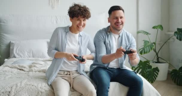 Linda pareja novio y novia jugando videojuego sentado en la cama en el dormitorio — Vídeos de Stock