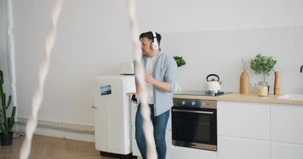 Bonito cara dançando na cozinha usando fones de ouvido segurando smartphone — Vídeo de Stock