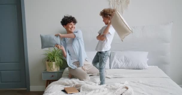 Young woman and small boy enjoying pillow fight on bed in apartment