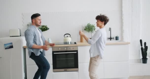 Joyful man och kvinna i casual kläder dansar skrattar i köket i lägenhet — Stockvideo