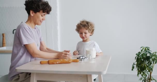 Mujer joven cocinando pastelería con niño pequeño en cocina en apartamento — Vídeos de Stock