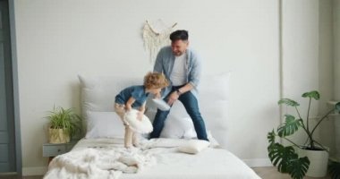 Baba ve oğul yatakta oynarken yastıklarla kavga ediyor sonra anne eve geliyor