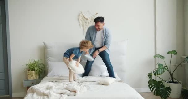 Padre e hijo jugando en la cama peleando almohadas cayendo luego madre volviendo a casa — Vídeo de stock