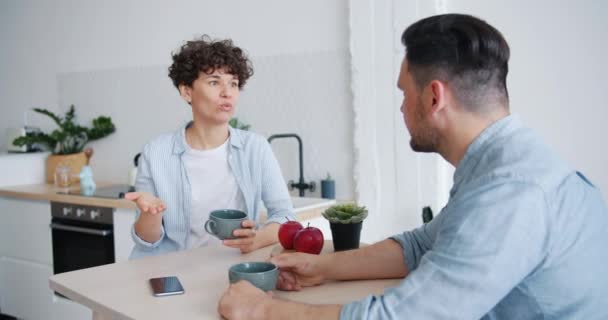 Δυσαρεστημένο ζευγάρι άντρας και γυναίκα που κάθεται στο τραπέζι στην κουζίνα μιλάει — Αρχείο Βίντεο