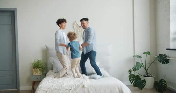 Movimento lento da família mãe pai filho pulando na cama no quarto se divertindo — Vídeo de Stock