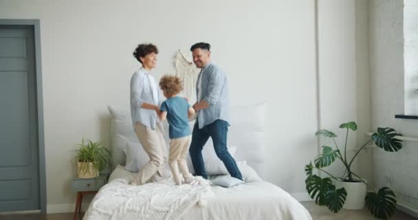 Mouvement lent de la famille mère père fils sautant sur le lit dans la chambre à coucher avoir du plaisir — Video