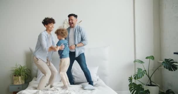 Madre padre e hijo saltando bailando en la cama en el dormitorio en casa juntos — Vídeo de stock