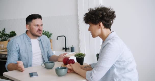 Powolny ruch zły człowiek krzyczeć w nieszczęśliwy żona siedzący w kuchnia w tabela — Wideo stockowe