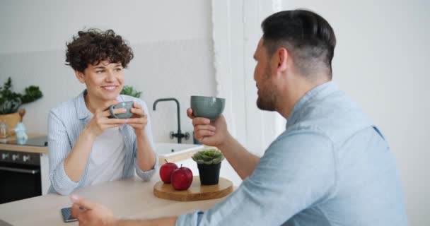 Meisje en kerel praten drinken koffie lachen thuis bij keuken tafel — Stockvideo