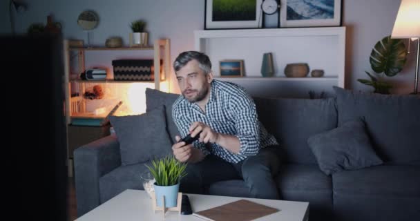 Homem jogando videogame e mastigando pipocas desfrutando de lazer à noite — Vídeo de Stock