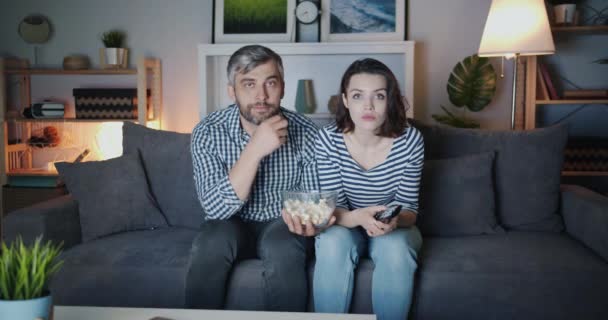 Retrato de pareja joven viendo noticias de última hora en la televisión por la noche expresando su conmoción — Vídeos de Stock