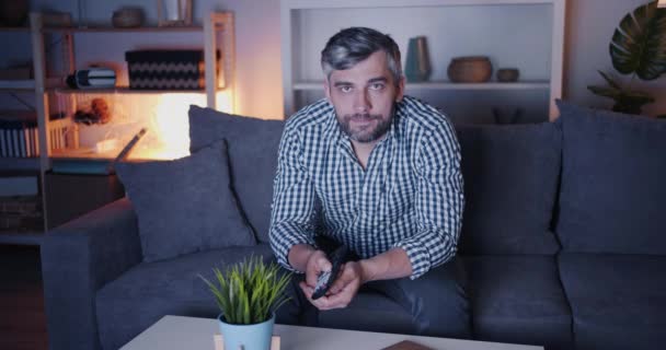 Retrato del hombre guapo viendo la televisión por la noche en casa mirando la cámara — Vídeo de stock