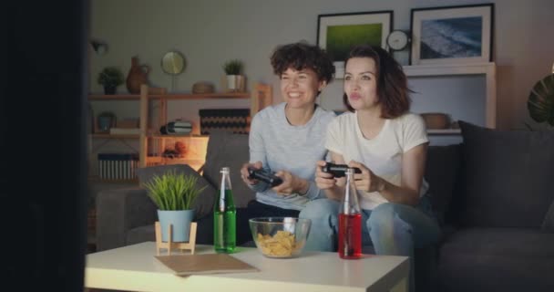 Belle ragazze che giocano a videogiochi a casa di notte divertendosi seduti sul divano — Video Stock