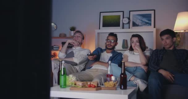 Multi-racial group of young people watching TV in dark apartment sitting on sofa — Stock Video