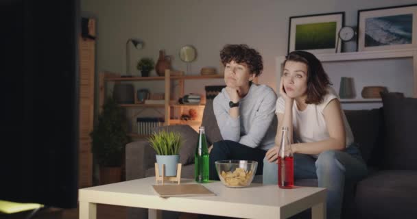 Female friends watching boring film on TV yawning sitting on couch at night — Stock Video