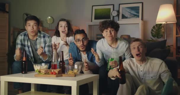 Happy friends doing high-five and clinking bottles watching sports on TV at home — Stock Video
