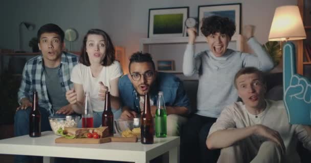 Alegre joven viendo deportes en la televisión apoyando haciendo chocar los cinco en la noche — Vídeo de stock