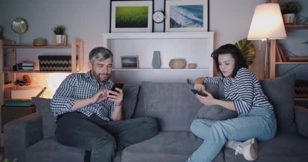 男人和女人在晚上在家里的电视机前使用智能手机 — 图库视频影像