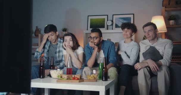 Personas cansadas hombres y mujeres viendo la televisión por la noche y comiendo bocadillos en casa — Vídeo de stock