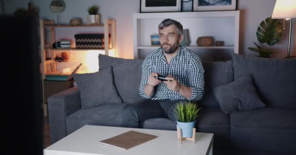 Barbudo cara desfrutando de vídeo game em casa à noite no sofá segurando joystick — Vídeo de Stock