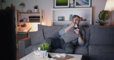 Sakallı adam televizyon izlerken patlamış mısır yiyor ve burun dokusuyla siliyor