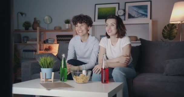 Pretty women watching TV laughing having fun at night in modern apartment — Stock Video