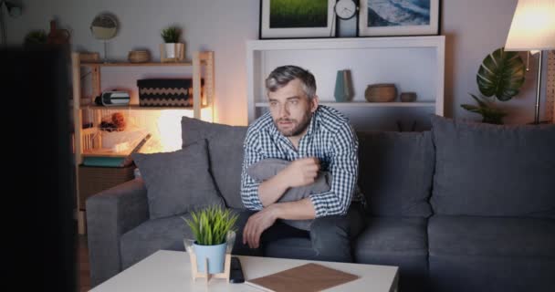 Homem alegre assistindo TV em casa comendo pipocas e rindo à noite sozinho — Vídeo de Stock