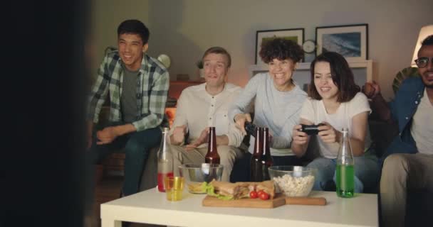 Girls playing video game while guys cheering doing high-five at night at home — Stock Video