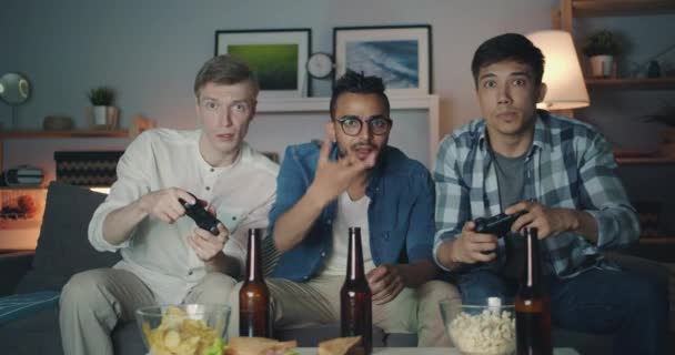 Портрет щасливих чоловіків, які грають у відеогру вдома вночі, дивлячись на камеру — стокове відео