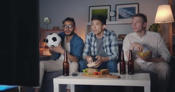 Chicos emocionales viendo el partido de fútbol en la televisión comiendo bocadillos celebrando la victoria — Vídeos de Stock