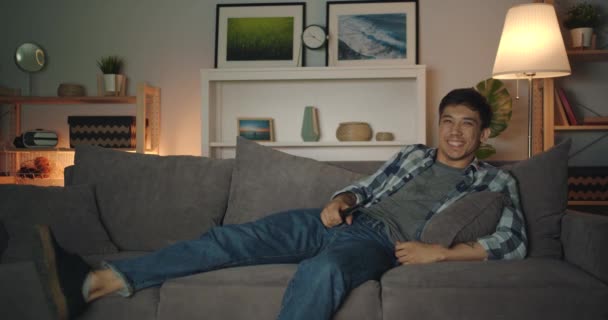 Joyful misto homem de raça se divertindo em casa assistindo TV rindo à noite — Vídeo de Stock