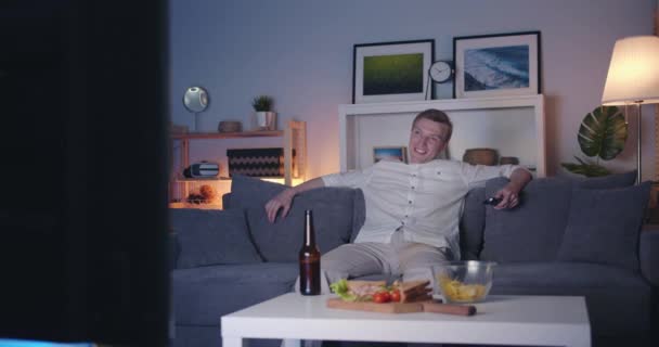 Joyful man tittar på TV hemma skrattar på soffan på natten njuter komedi ensam — Stockvideo