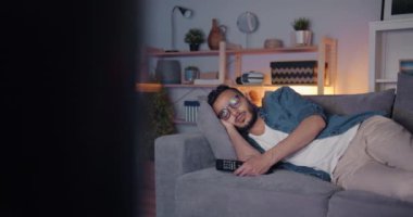 Yorgun Orta Doğulu adam tv önünde kanepede tek başına yatarken uyuyor