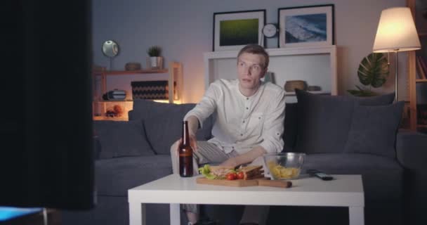自宅で夜にビールをこぼして飲むテレビを見てショックを受けた男 — ストック動画